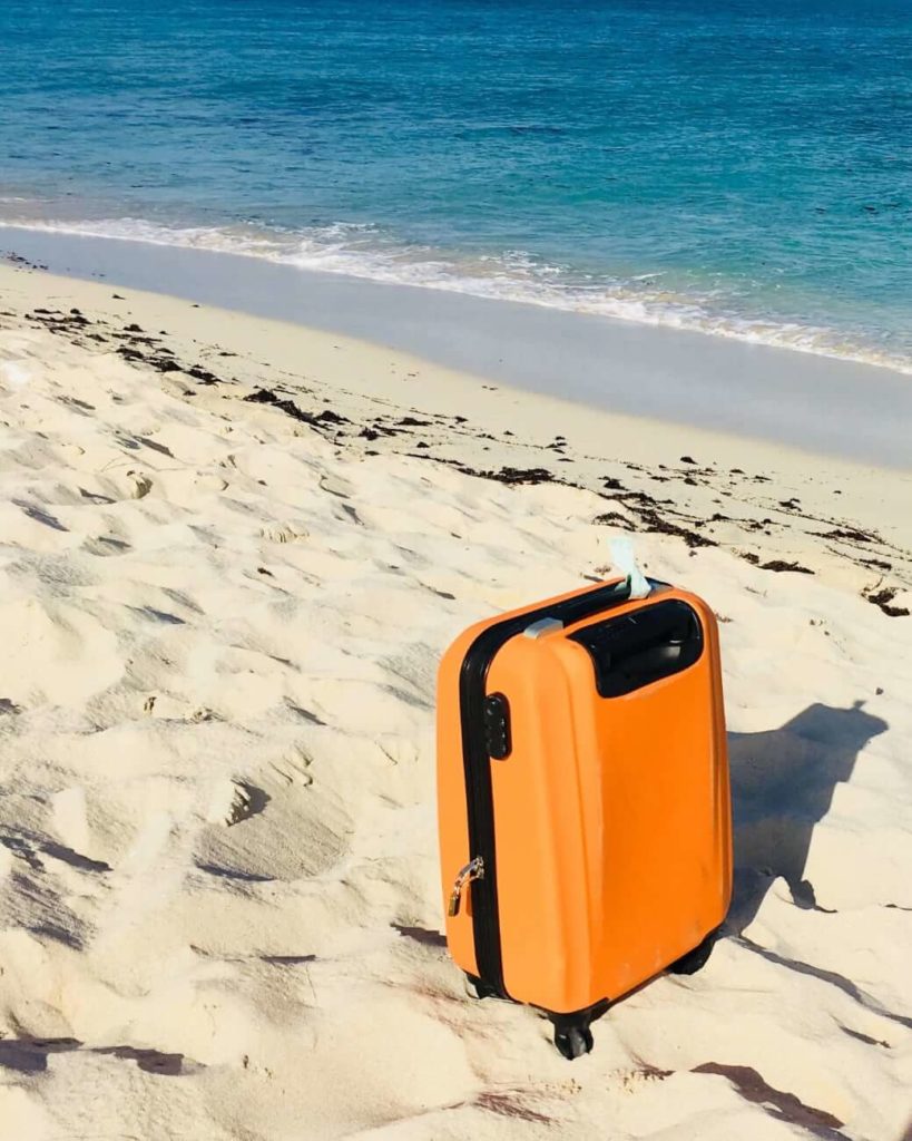 Orange roller suitcase on sandy beach with deep blue water