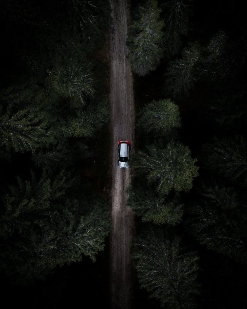 photo from above of white and black car on road at night through green trees