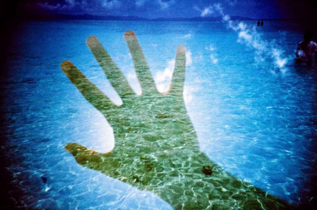 Photo of cerulean beach water double-exposed with an image of a hand blocking the sun