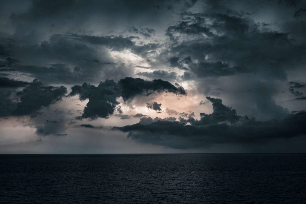 Photo of diffused sunlight trapped in swirling, ominous storm clouds over the ocean