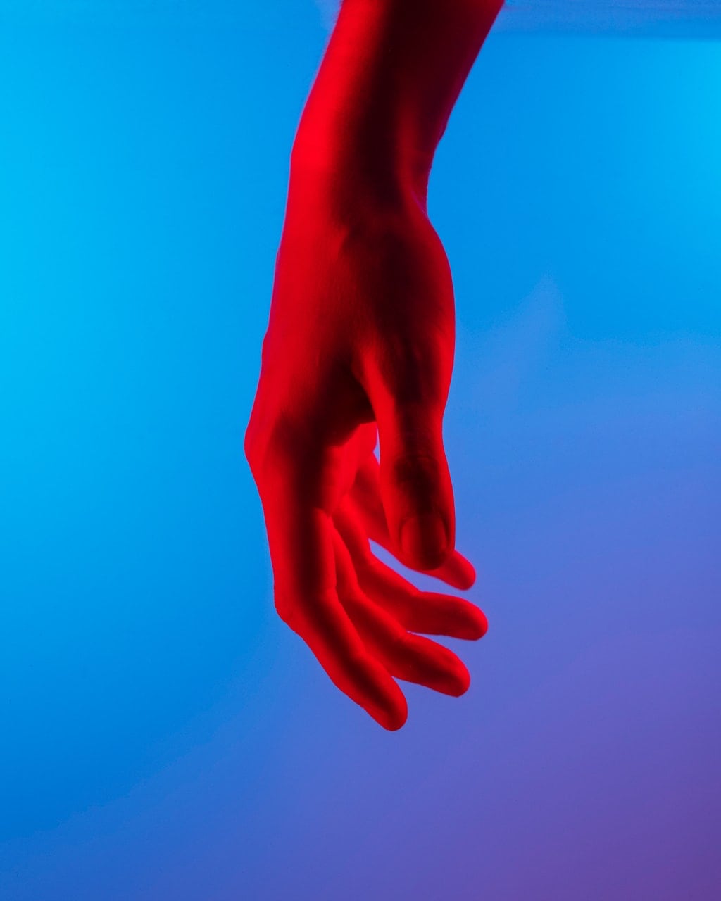 Photo of right hand lit red against blue background.